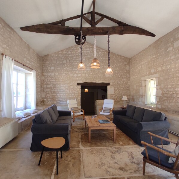 A rustic room with stone walls, wooden beams, a fireplace, and two sofas.