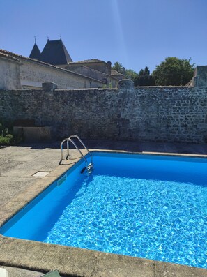 A swimming pool with a stone wall and a metal ladder.