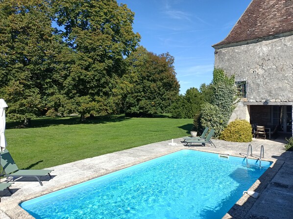 A swimming pool with a grassy lawn and trees in the background.