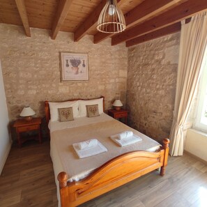 A bedroom with a wooden bed, two bedside tables with lamps, a stone wall, and a framed certificate on the wall. - Le Pressoir du Château de Clerbise—a spacious, charming vacation home with a private pool (Belluire)