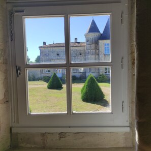 A window with a view of a building with multiple windows and a lawn with two trimmed bushes. - Le Pressoir du Château de Clerbise—a spacious, charming vacation home with a private pool (Belluire)