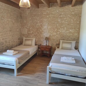 A room with two single beds, wooden floors, a stone wall, and a hanging light fixture.