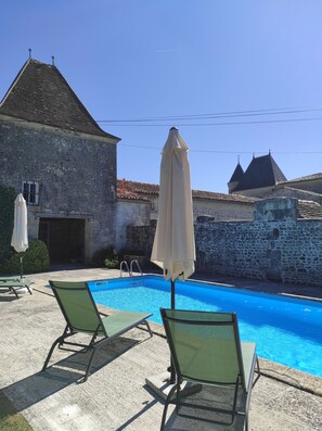 A swimming pool with lounge chairs and umbrellas, surrounded by stone buildings with tiled roofs. - Le Pressoir du Château de Clerbise—a spacious, charming vacation rental with a private pool (Belluire)