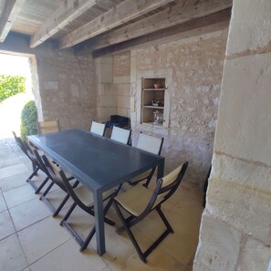 An outdoor dining area with a long table and chairs, a stone wall, and a shelf with kitchenware. - Le Pressoir du Château de Clerbise—a spacious, charming vacation rental with a private pool (Belluire)