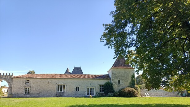 A stone building with a tiled roof and a small tower, surrounded by a grassy area.
