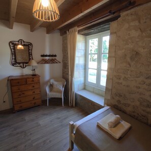 A room with a wooden dresser, a chair, a window with curtains, and a bed with a towel.