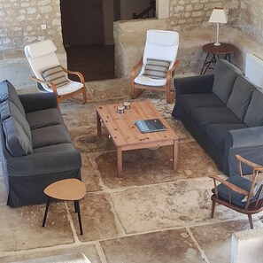 A living room with a stone floor, a wooden coffee table, a sofa, two armchairs, and a small side table with a lamp.