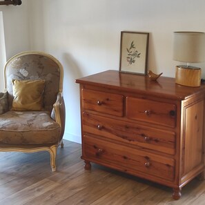 A wooden dresser with drawers, a chair with a floral pattern, and a framed picture on the wall.