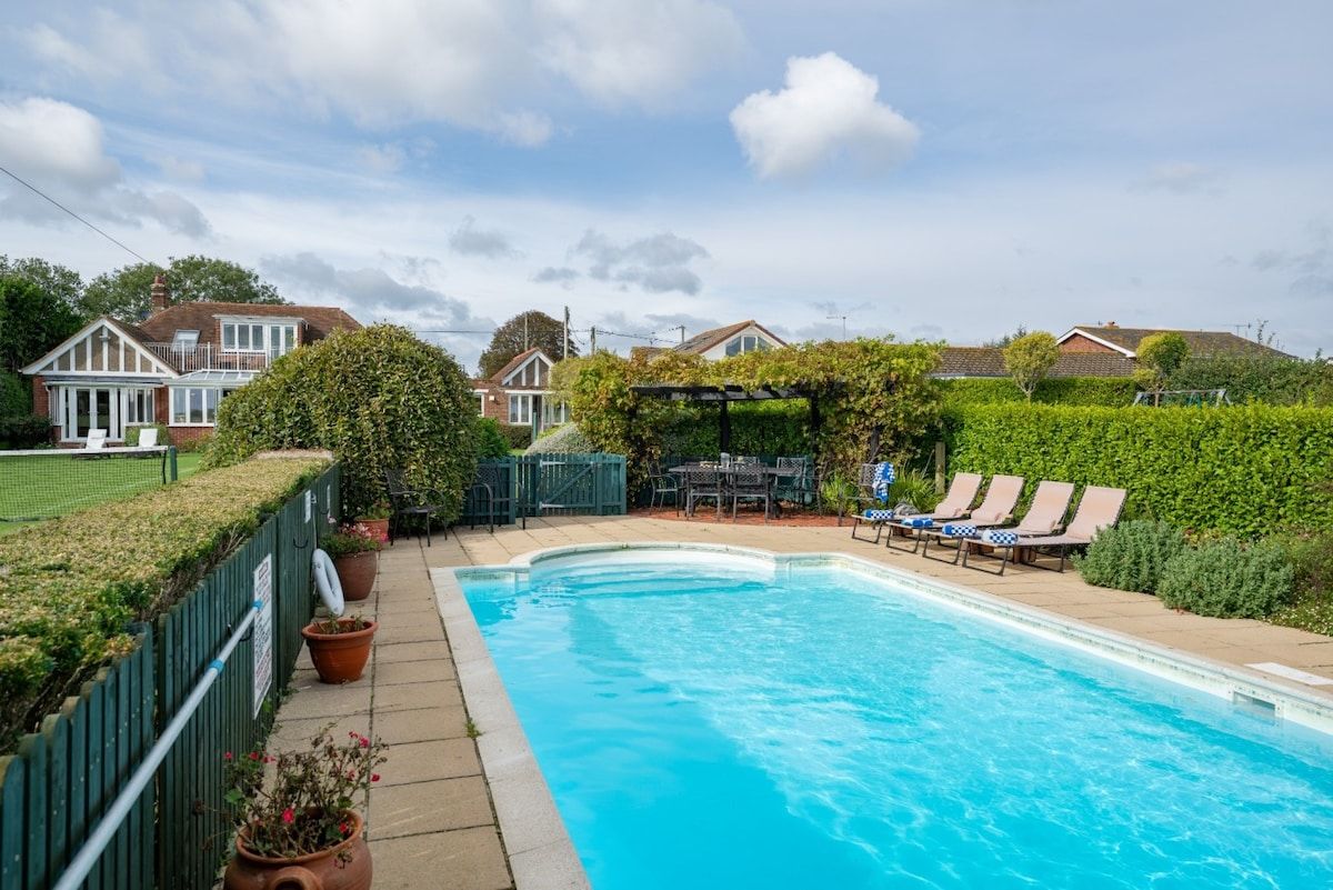 Une piscine dotée de chaises longues et d’une pergola, entourée d’une haie et d’une clôture.