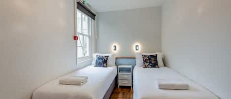 A small, narrow room with two single beds, a window, and a wooden floor.