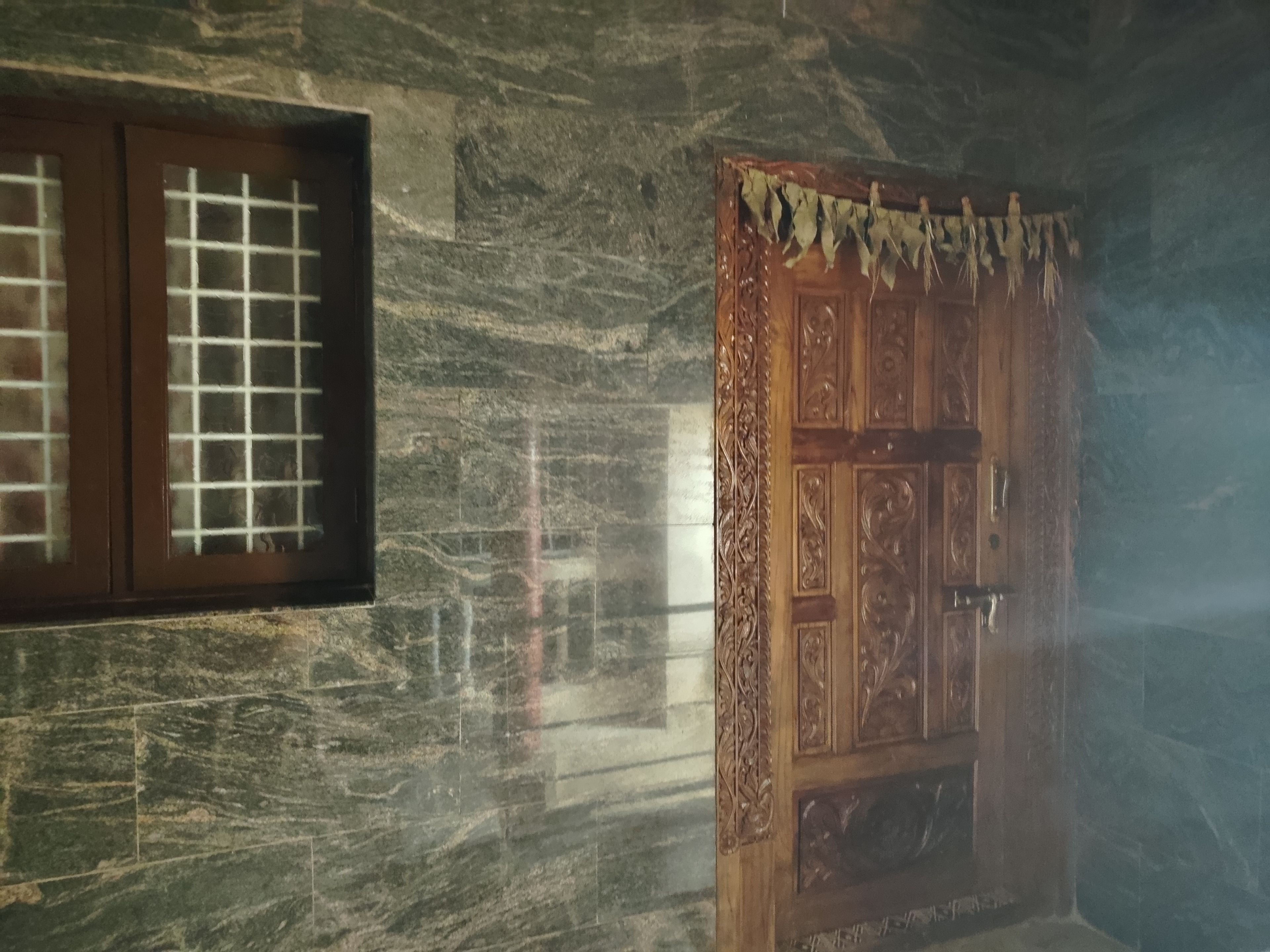 A room with a stone wall, a wooden door with intricate carvings, and a window with a grid pattern.