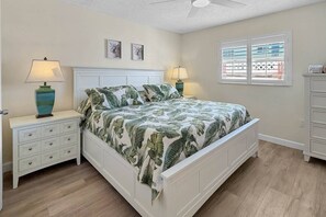 Ein Schlafzimmer mit einem Bett, Nachttischen, einer Kommode und einem Fenster mit Jalousien.
