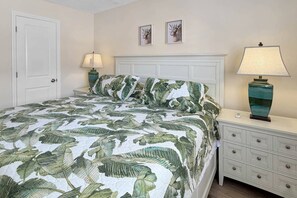 A bedroom with a bed, nightstand, lamp, dresser, and two framed pictures on the wall. - Ground Floor Beachfront Condo. Heated Pool. Shuffleboard. Perfect Location. No Car Necessary! (Treasure Island)