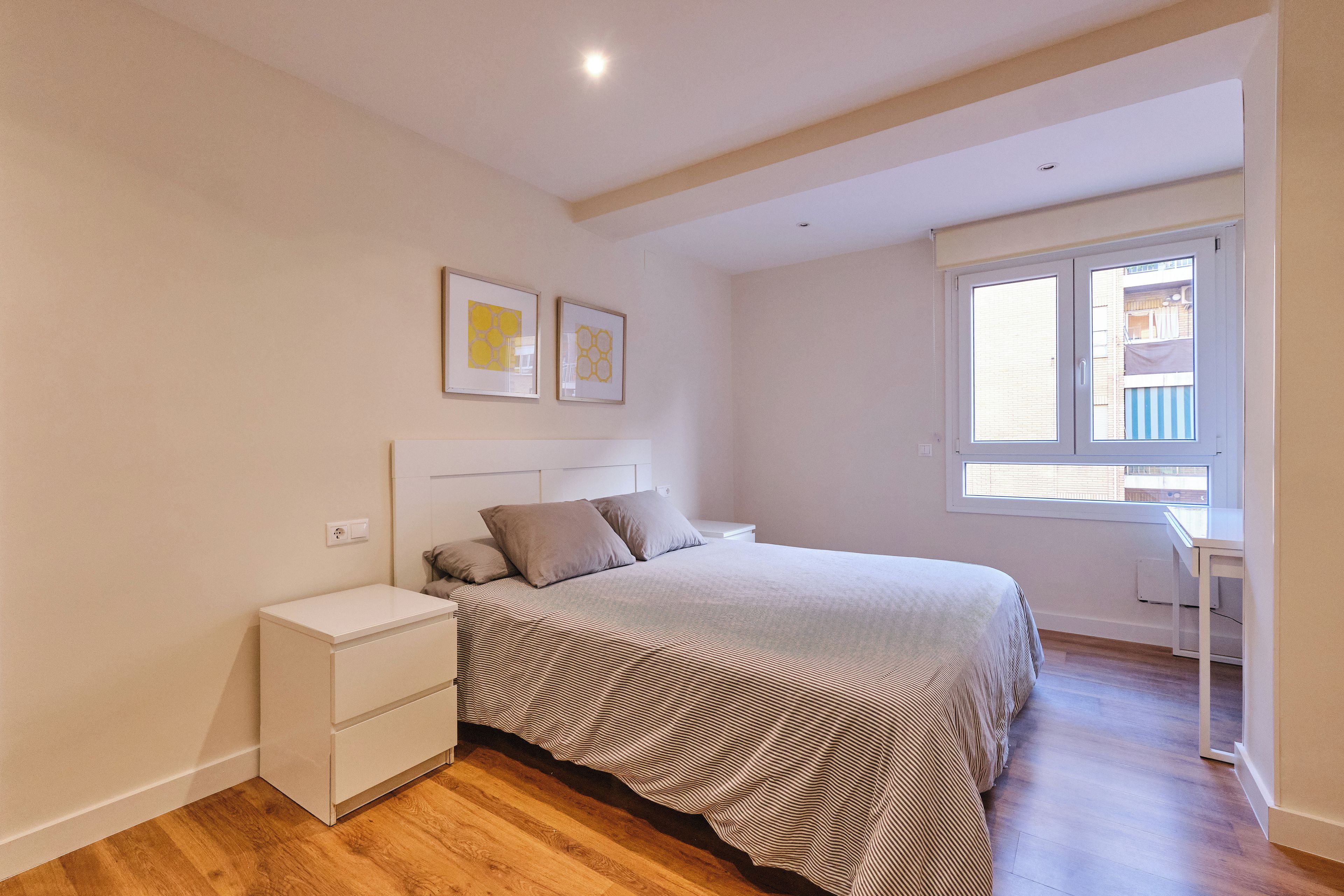 Une chambre à coucher avec un lit, des tables de chevet, une fenêtre et des œuvres d’art accrochées au mur.