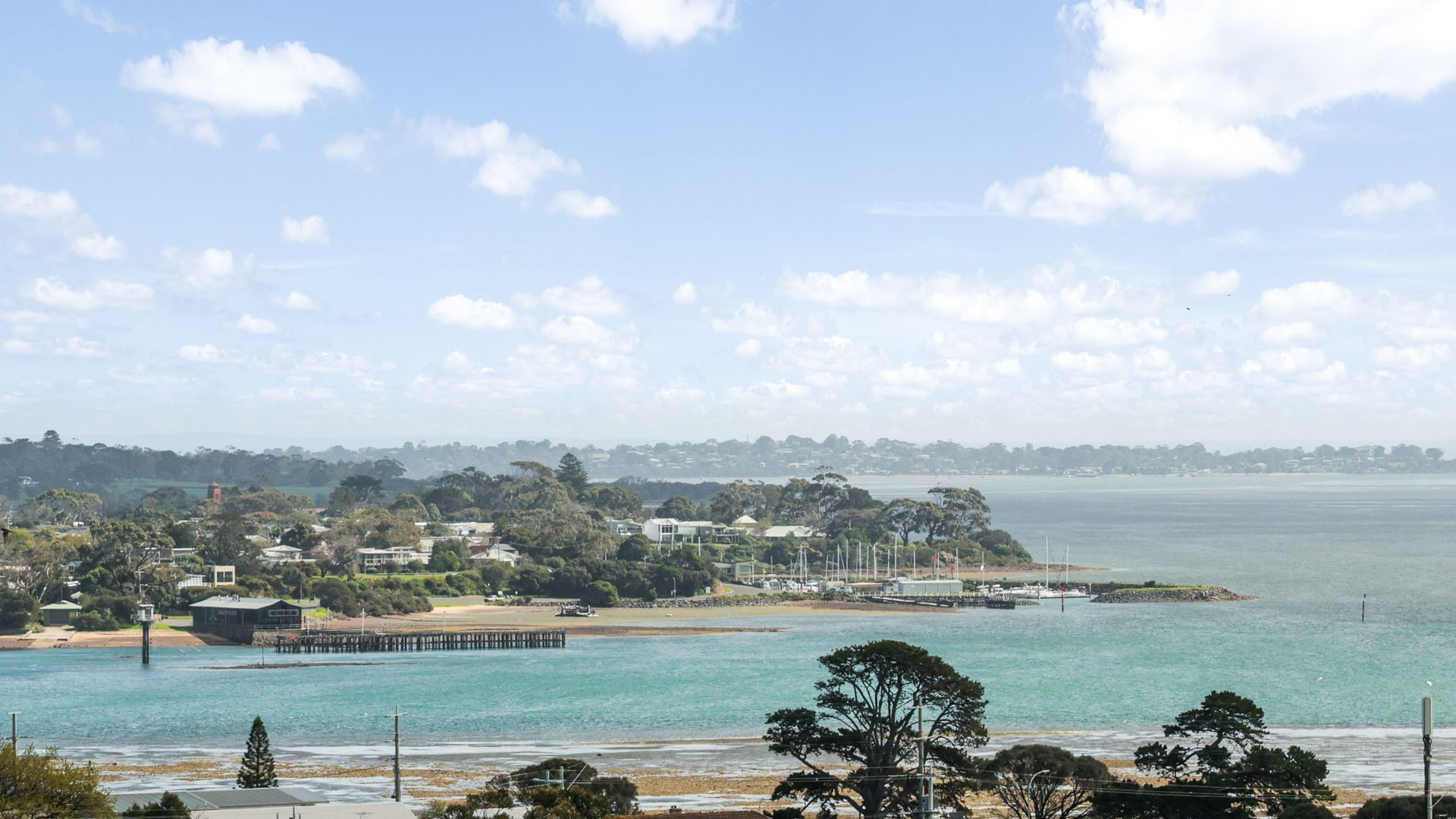 A coastal town with a pier extending into the sea, surrounded by residential buildings and greenery.