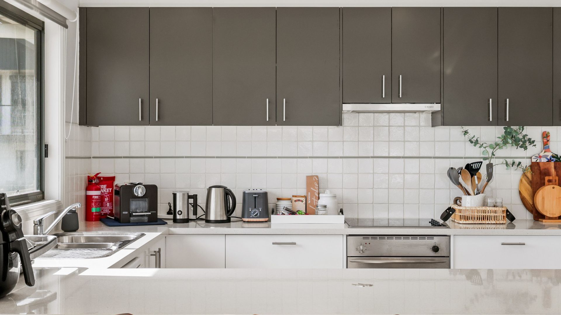A modern kitchen with dark cabinets, a coffee machine, a kettle, and various utensils on the counter.
