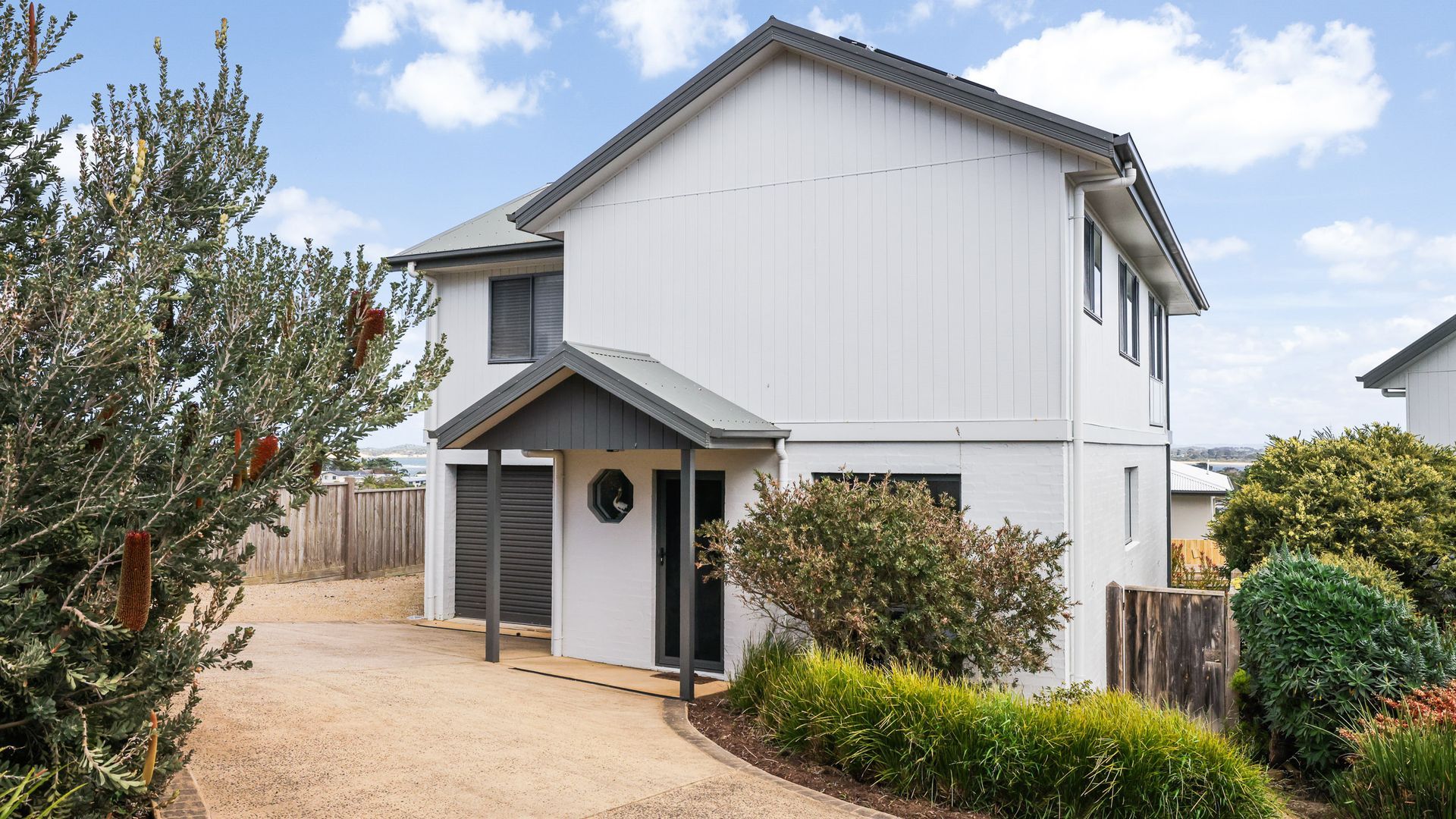 A two-story residential building with a driveway, a front door, and a small porch.