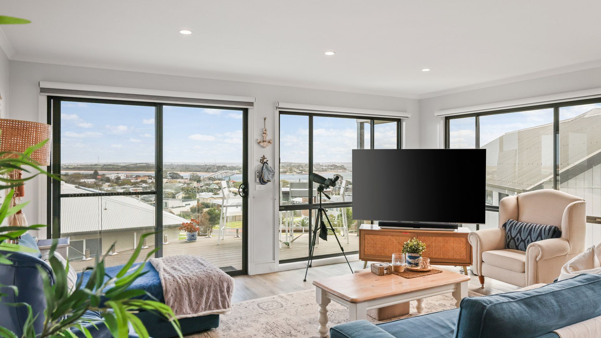 A spacious living room with a large TV, comfortable seating, and a balcony with a city view.