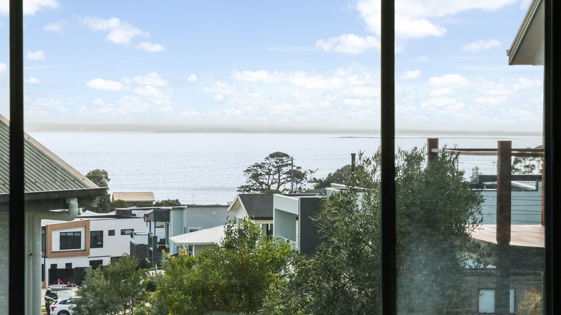 A residential area with modern houses, a view of the sea, and a clear sky.