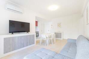 Ein modernes Wohnzimmer mit einem Flachbildfernseher, einem grauen Sofa und einem Essbereich mit weißen Stühlen.