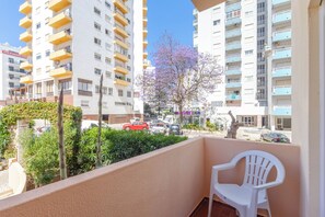 Ein Balkon mit einem weißen Plastikstuhl, ein Baum mit violetten Blüten und ein Parkplatz mit Autos.