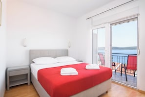 A bedroom with a bed, a nightstand, a balcony with chairs, and a view of the sea. - A1 - apartment with shared pool & balcony, next to the beach (Mastrinka)