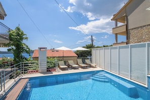 A swimming pool with lounge chairs and a view of a building with a red-tiled roof. - A1 - apartment with shared pool & balcony, next to the beach (Mastrinka)