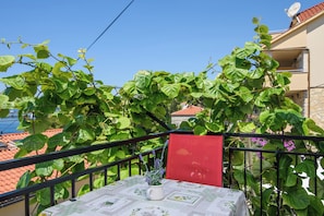 A balcony with a table, a red chair, and a white vase with flowers. - A1 - apartment with shared pool & balcony, next to the beach (Mastrinka)