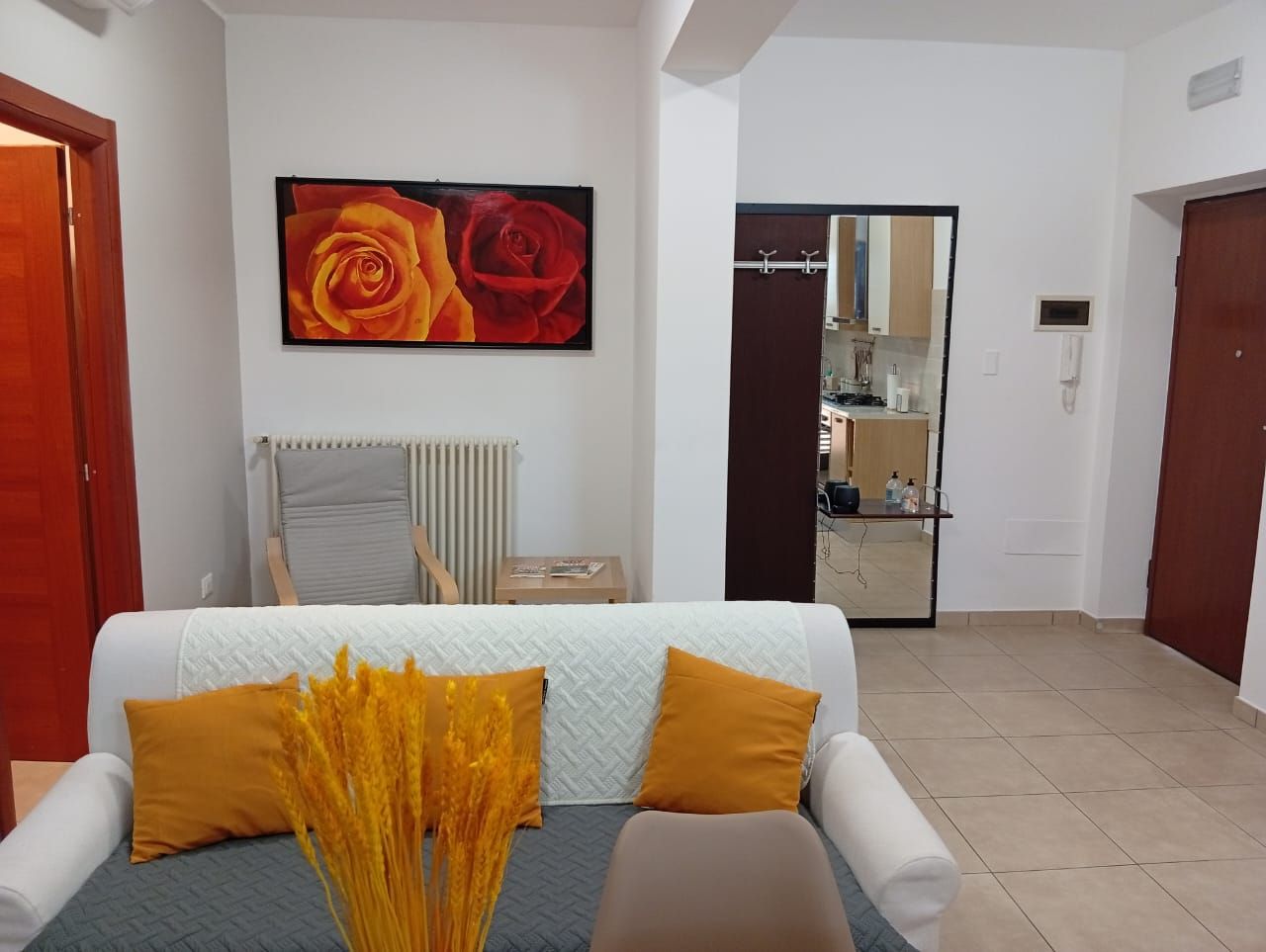 A modern living room with a sofa, a large painting of roses, a radiator, and a view into the kitchen.