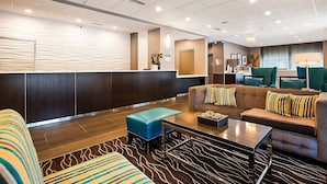 A modern lobby with a reception desk, seating area, and a dining section.