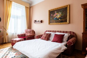 A bedroom with a large bed, two armchairs, a wooden cabinet, and a painting on the wall. - Charming 2BR Apt. near the National Museum by EasyBNB Premium (Prague)