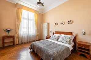 Ein Schlafzimmer mit einem großen Bett, Holznachttischen, einer Kommode und einem Fenster mit Vorhängen.