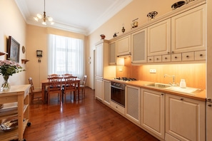 A kitchen with wooden cabinets, a dining table with chairs, a chandelier, and a window with sheer curtains. - Charming 2BR Apt. near the National Museum by EasyBNB Premium (Prague)
