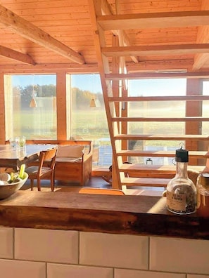 A wooden interior with a dining area, a bottle of liquor, and a view of the outdoors.