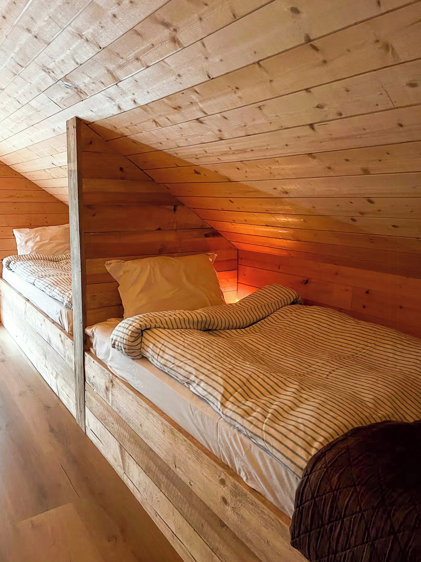 A single wooden bed in a cabin-style room with a sloped ceiling.