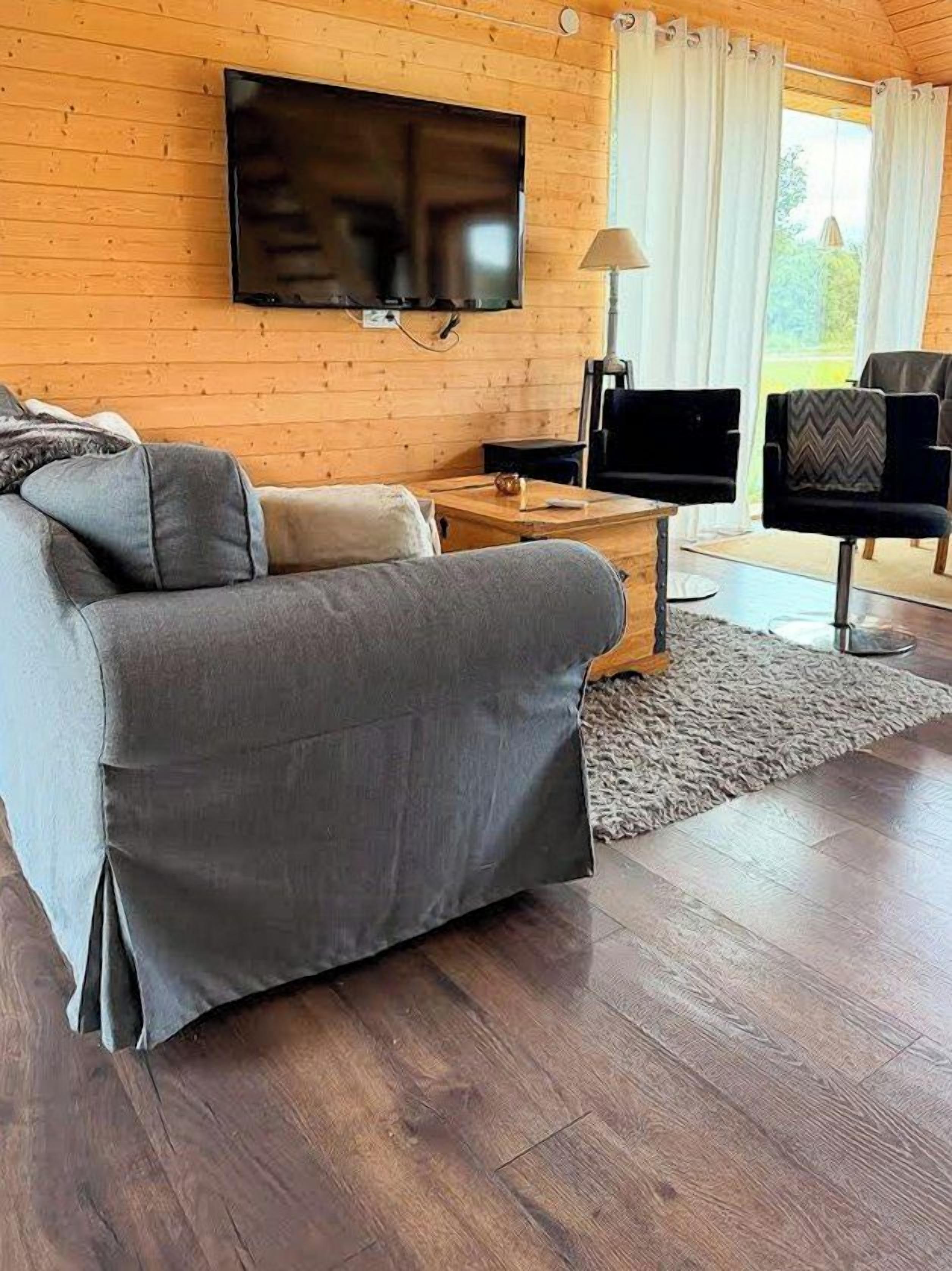 Een woonkamer met een bank, een salontafel, een aan de muur bevestigde televisie en een raam met gordijnen.