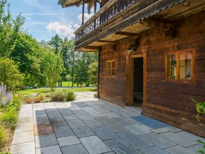 Eine Holzhütte mit Balkon, einem Steinweg und umgebender Bepflanzung.