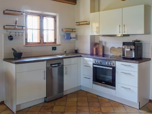 A kitchen with white cabinets, a dishwasher, an oven, and a coffee machine.