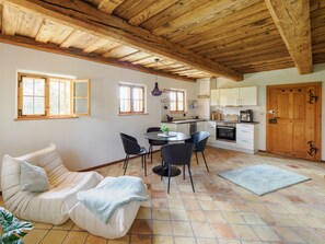 A cozy kitchen with wooden beams, a dining area with chairs, and a sofa.