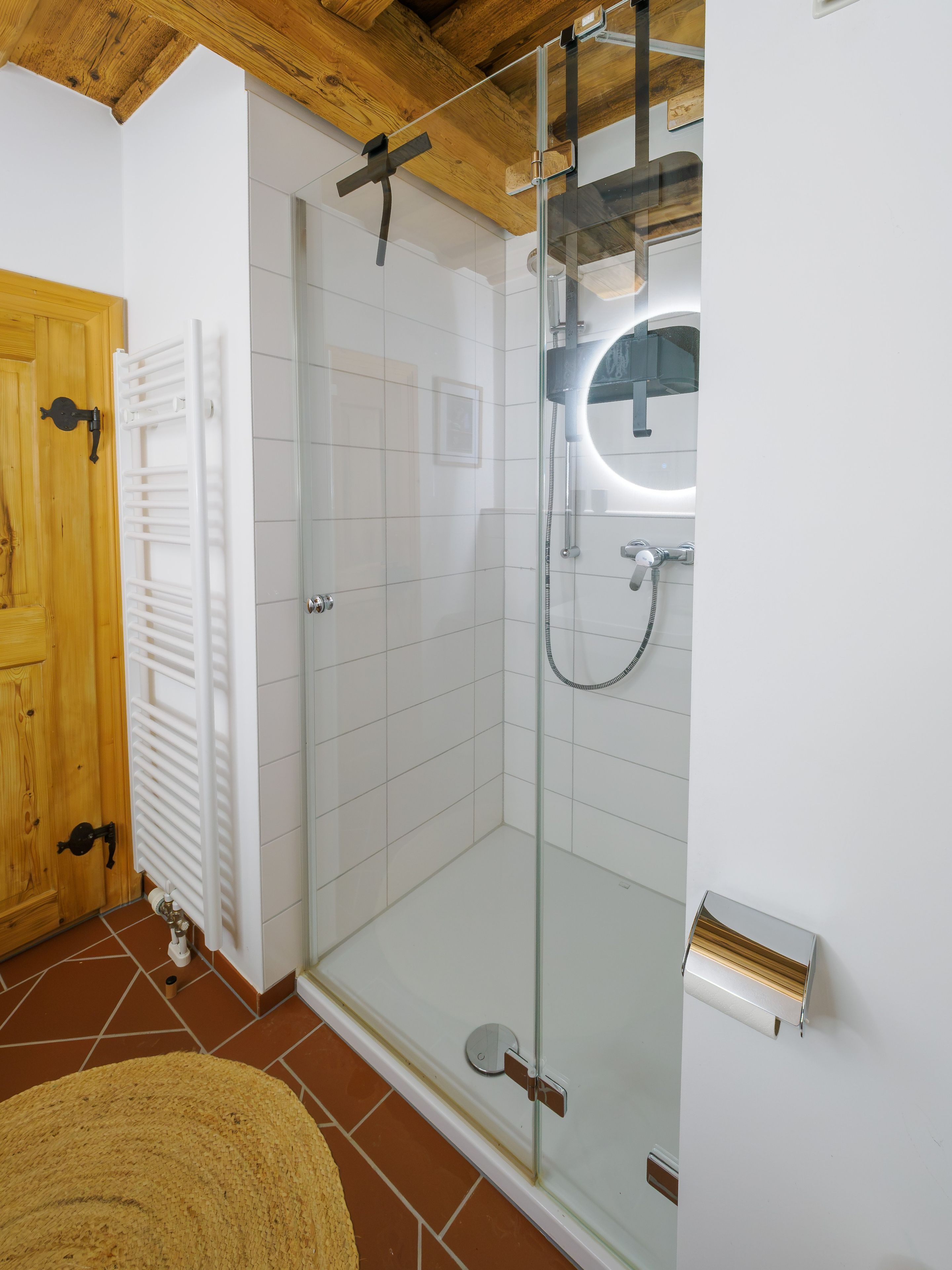 Une salle de bain moderne avec une douche à parois de verre, un radiateur blanc et une porte en bois.
