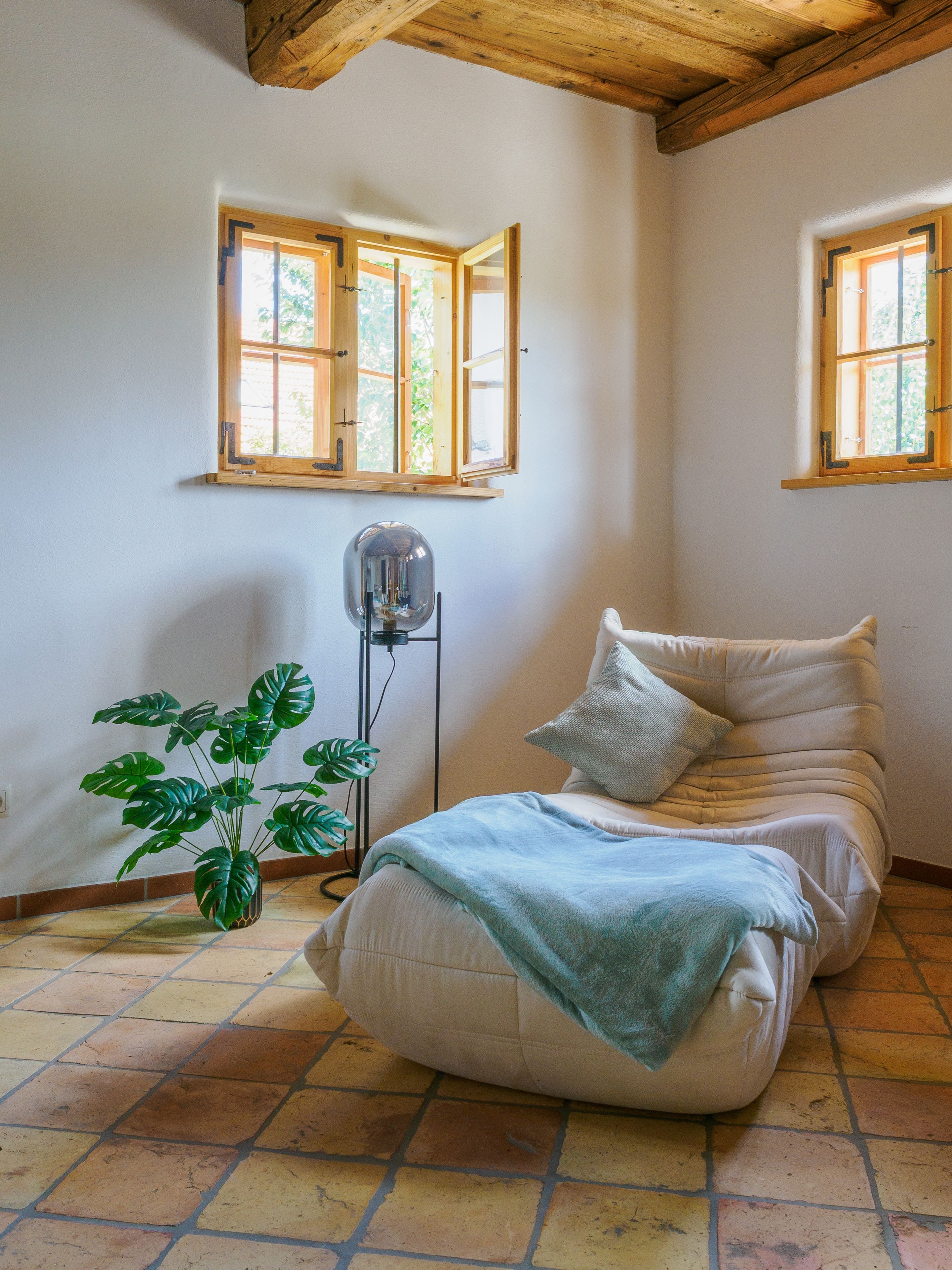 Une chambre à coucher avec un lit, une plante en pot et deux fenêtres.