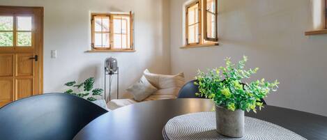 A dining area with a round table, chairs, a potted plant, and wooden beams on the ceiling.