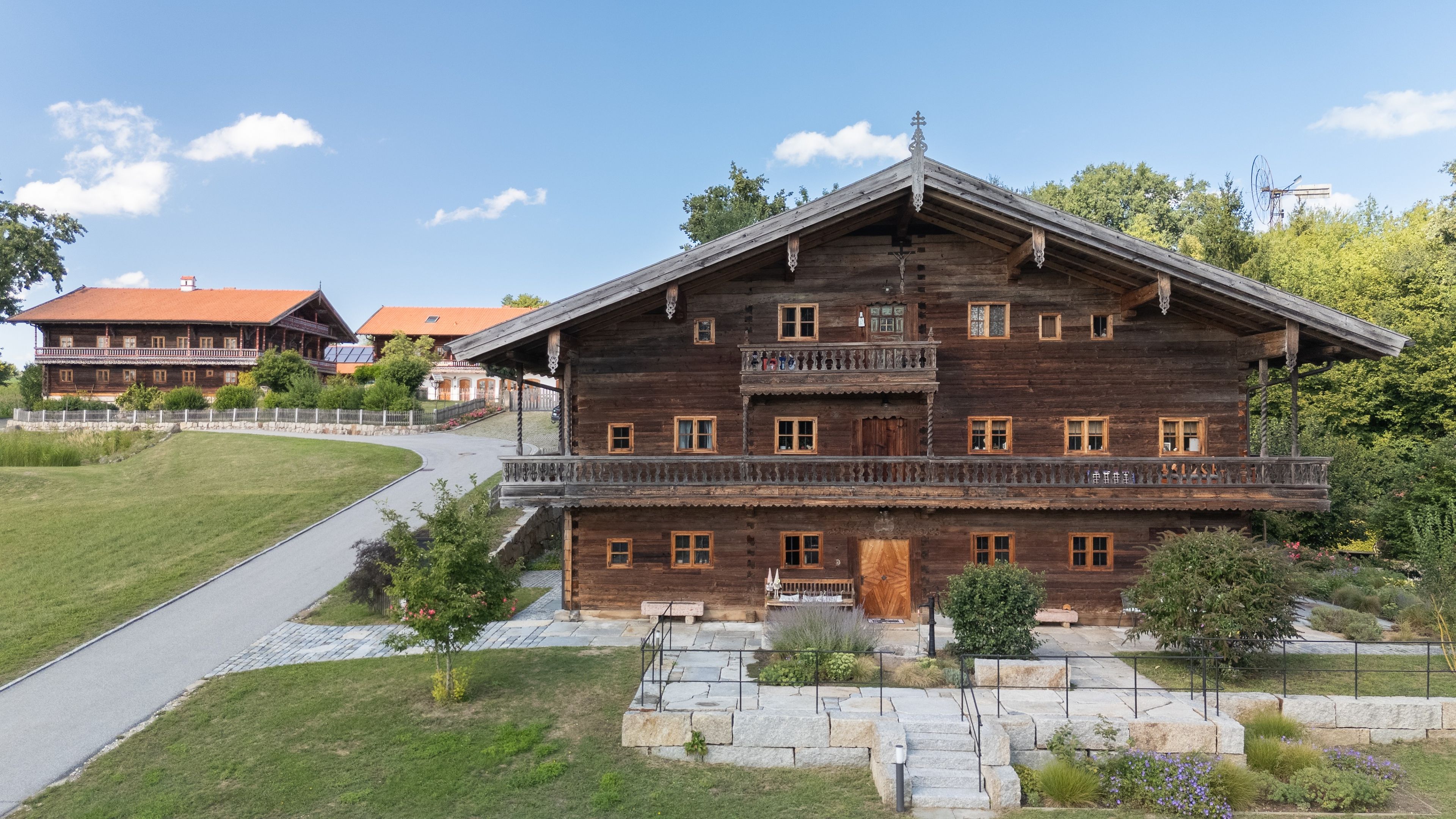A large wooden building with multiple balconies, a paved driveway, and a well-maintained lawn.