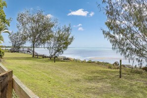 A grassy area with a wooden bridge leading to a beach, surrounded by trees and a clear sky. - HiTide at Toogoom | Stunning Views | Air-Con | Beach Access | Linens | Pets (Toogoom)