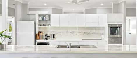 A modern kitchen with white cabinetry, a marble countertop, a built-in oven, and a ceiling fan.