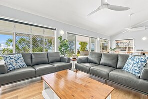 A spacious living area with two leather sofas, a wooden coffee table, and large windows offering views of greenery and a building. - HiTide at Toogoom | Stunning Views | Air-Con | Beach Access | Linens | Pets (Toogoom)