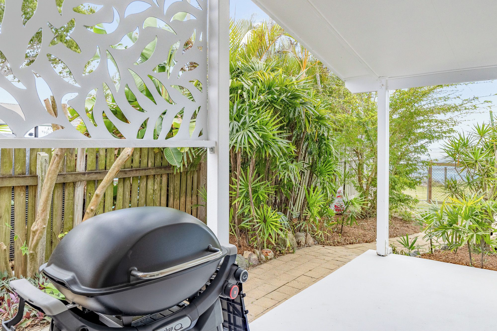 Un espace extérieur abrité, doté d’un barbecue, d’une clôture en bois et d’une végétation tropicale.