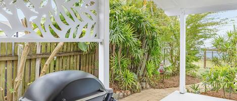 Un espace extérieur abrité, doté d’un barbecue, d’une clôture en bois et d’une végétation tropicale.