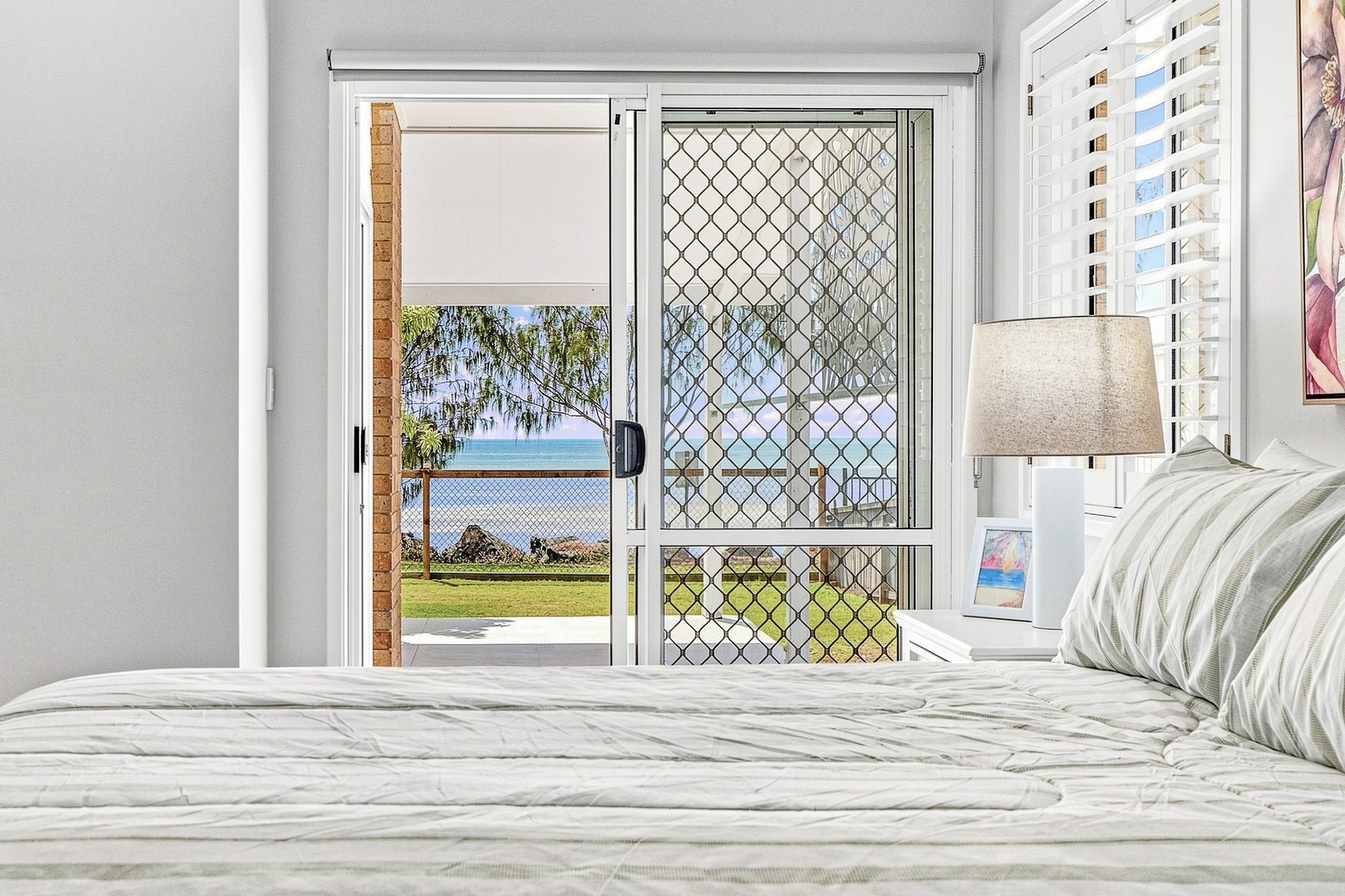 A bedroom with a bed, a nightstand, a lamp, and a view through a glass door to a balcony.