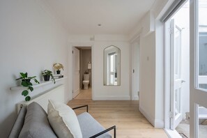 A hallway with a white radiator, a plant shelf, a mirror, and a door leading to a bathroom. - 2-bed Flat Near Regent s Park - Patio - Sleeps 6 (London)